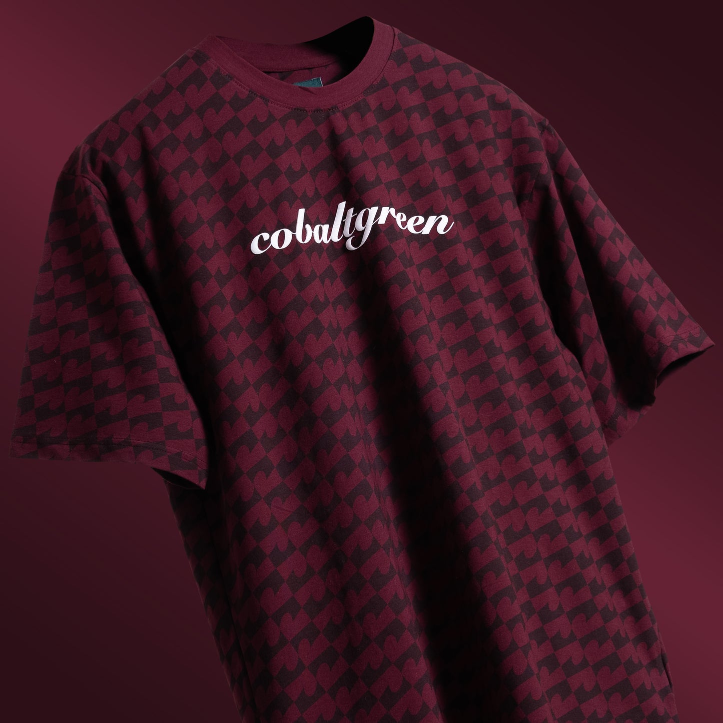 Maroon oversized t-shirt with an all-over-print design, floating against a matching maroon background for a tone-on-tone effect. The shirt features 'Cobalt green' branding on the chest plate, creating a subtle yet stylish look that emphasizes the seamless blend of color and design.