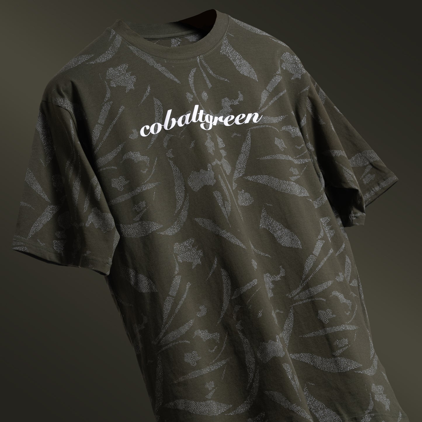 Olive oversized t-shirt with an all-over-print design, floating against a matching olive-toned background for a cohesive, monochromatic effect. The shirt is accented with 'Cobalt green' branding on the chest plate, offering a sleek and modern look.