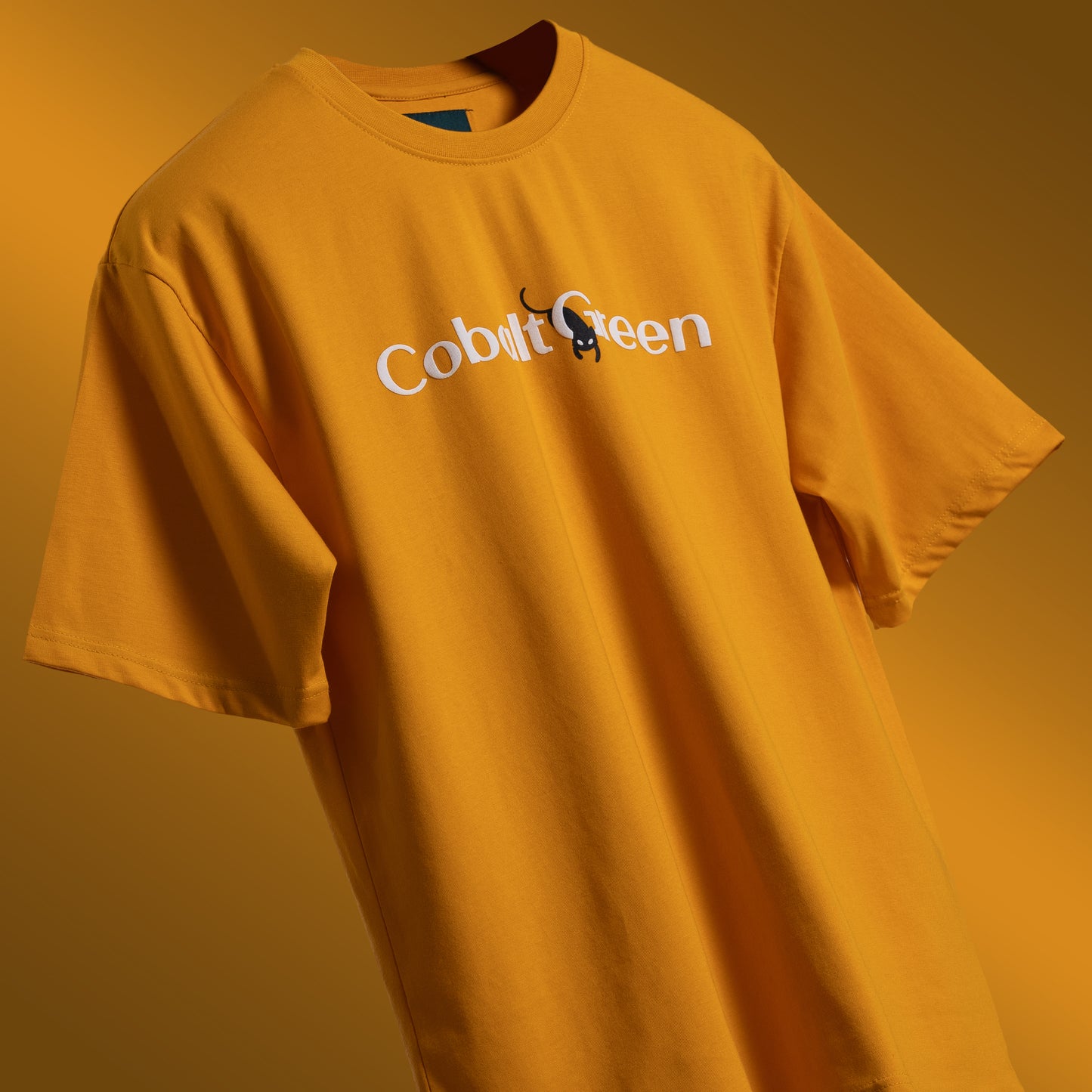 Vibrant yellow oversized 'Cat-Not Tee' floating against a clean backdrop, featuring 'Cobalt Green' branding on the front. The back displays playful screen and puff print artwork with the phrase 'I just cat-not stay awake' and a sleepy black cat graphic. Made from 220 GSM cotton-rich fabric, this tee offers a relaxed unisex fit, bio-washed and gold-finished for a soft, premium feel. Perfect for casual wear, lounging, or adding a humorous touch to any outfit.