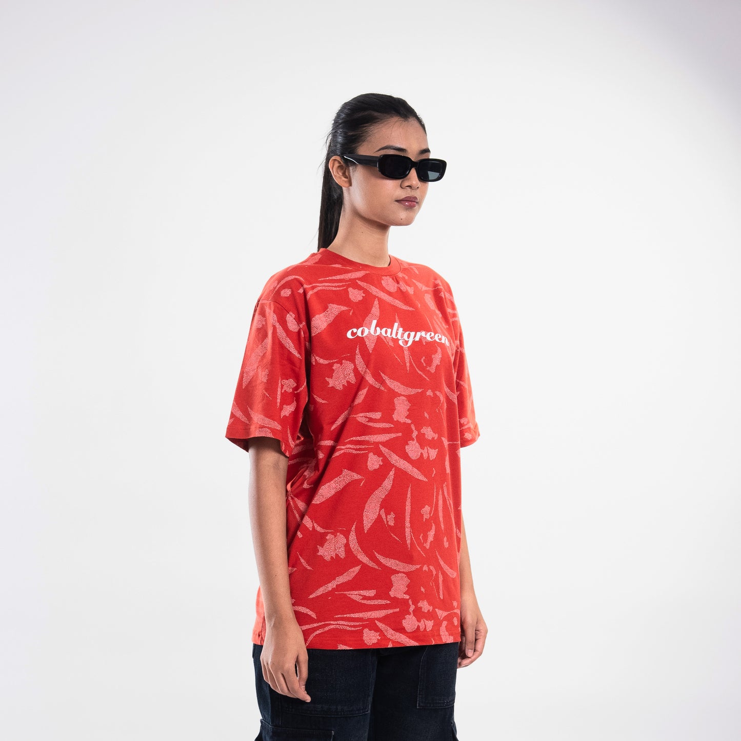 Female model, 5'10", wearing an oversized brick-red t-shirt with an all-over-print design. The relaxed fit drapes effortlessly, showcasing the 'Cobalt green' branding on the chest. A statement piece for a casual yet chic outfit.