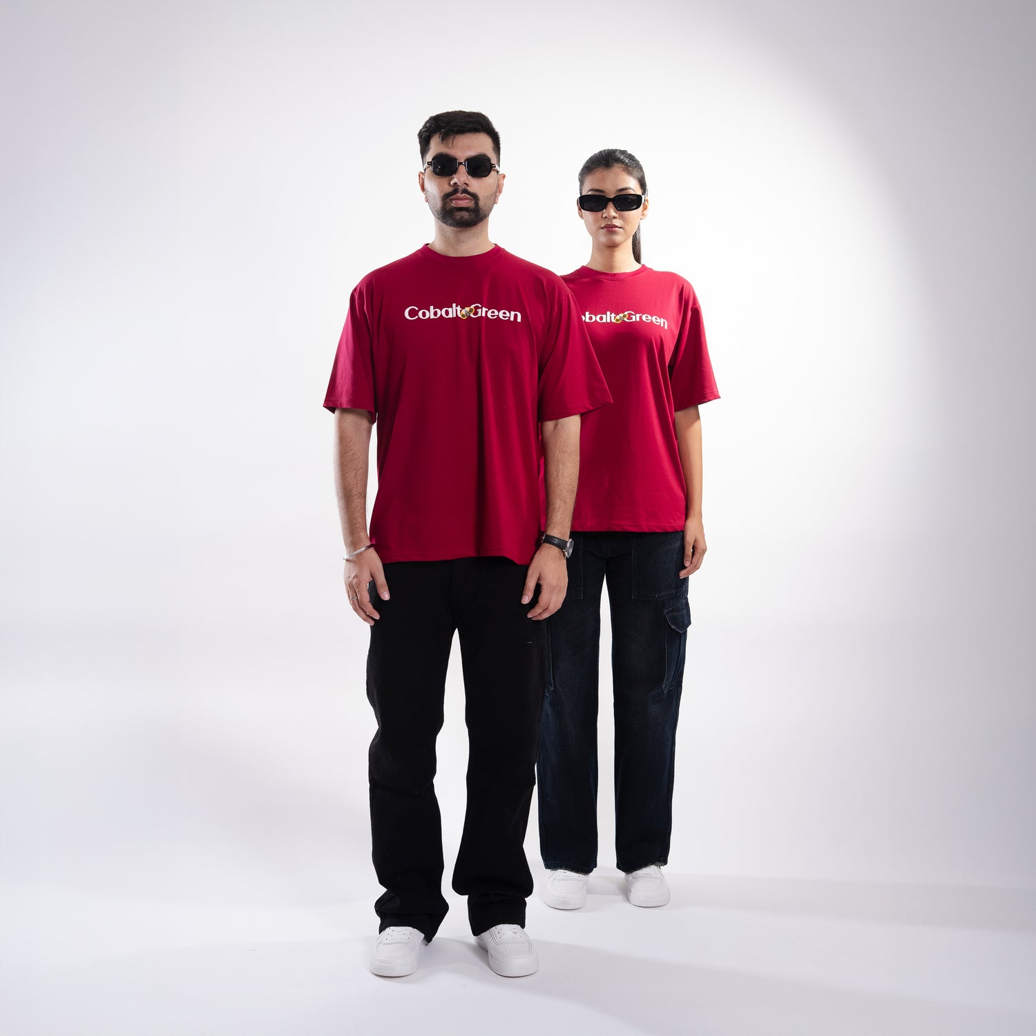 Male and female models, both 5'10", wearing the bold maroon 'Stop Bugging Me Tee' in a posed front shot. The front of the tee features 'Cobalt Green' branding, while the oversized fit provides a relaxed and flattering look. The playful design combines humor and comfort, making it a stylish statement piece for both models, perfect for casual outings or expressing a bit of attitude.