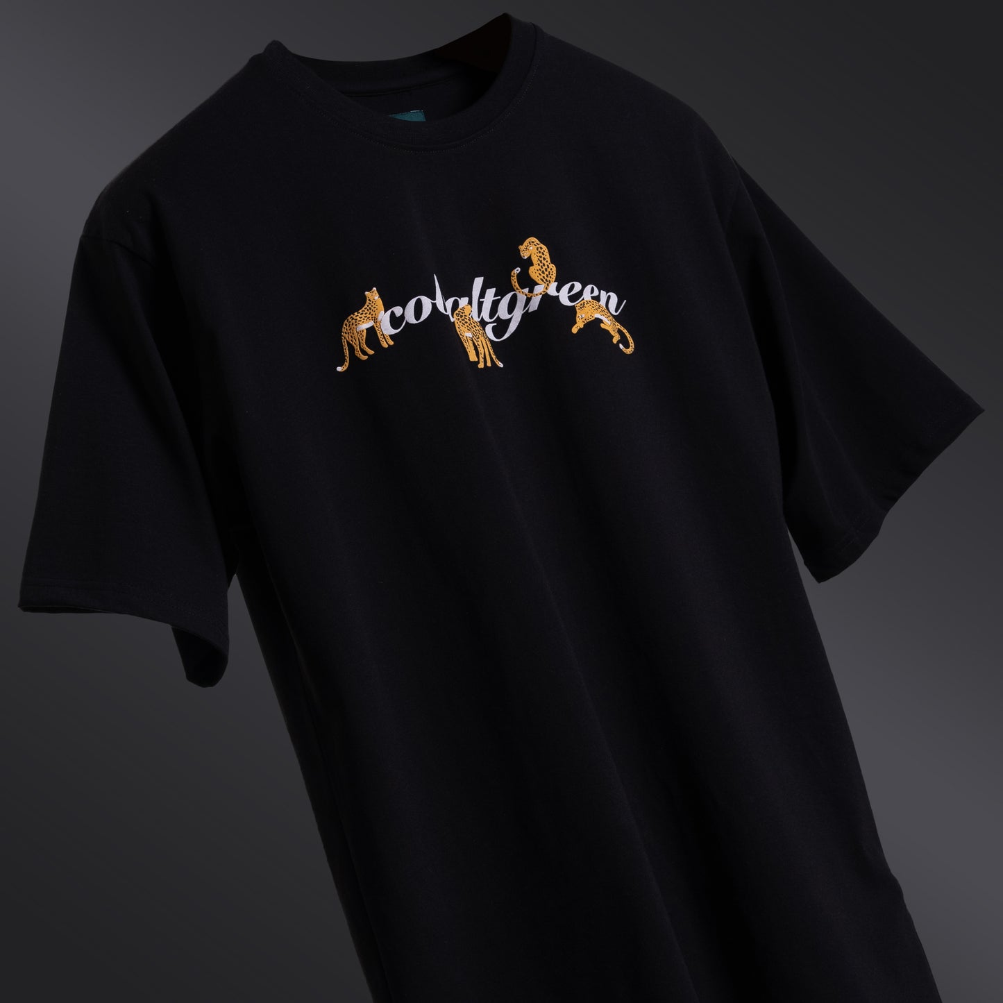 Classic black oversized 'Leopard Tee' floating against a matching backdrop, featuring a striking screen and puff print of a leopard and roses on both the front and back. The premium 220 GSM cotton-rich fabric ensures durability and comfort, while the bio-washed and gold-finished treatment provides a soft, luxurious feel. The relaxed, unisex fit offers a flattering look for all body types, making it the perfect choice for those seeking bold style with a touch of elegance.