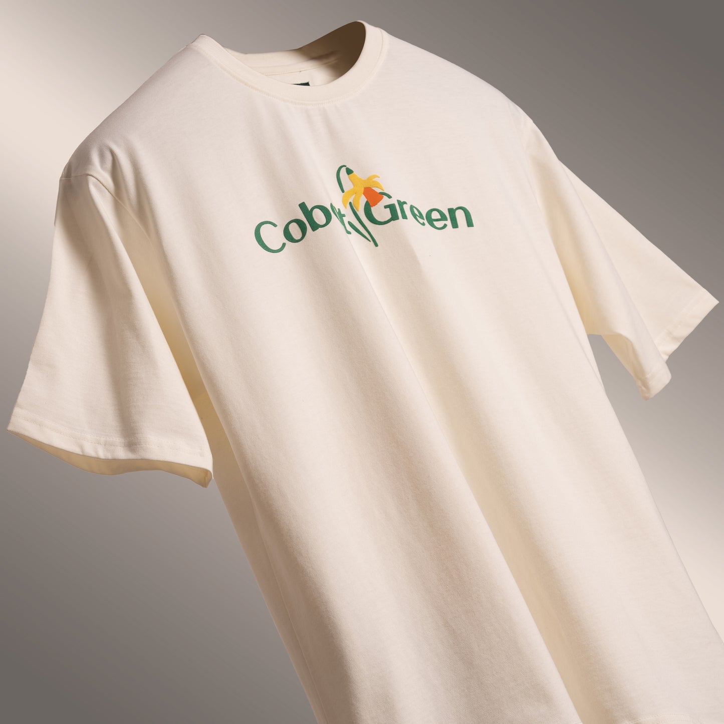 Off-white oversized 'Yellow Lily Tee' floating against a matching backdrop, featuring beautiful yellow summer lilies in screen and puff print on the front and back. Crafted from 220 GSM cotton-rich fabric with bio-washed and gold-finished treatment for a soft, premium feel. The unisex comfort fit offers a relaxed, flattering look, making this tee perfect for casual outings, weekend wear, or lounging in style.