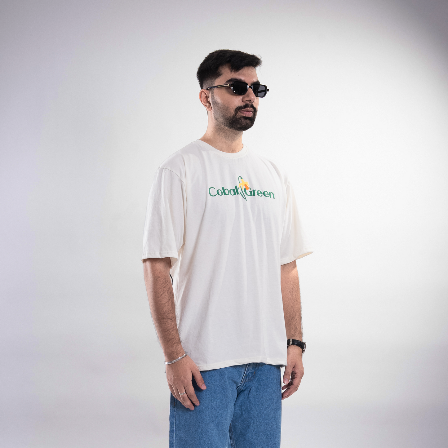 Male model, 5'10", wearing the off-white 'Yellow Lily Tee' in a mid shot. The tee features vibrant yellow summer lilies in screen and puff print on the front and back. The oversized, unisex fit offers a comfortable and stylish look, emphasizing the bold floral design and premium fabric, perfect for casual wear.