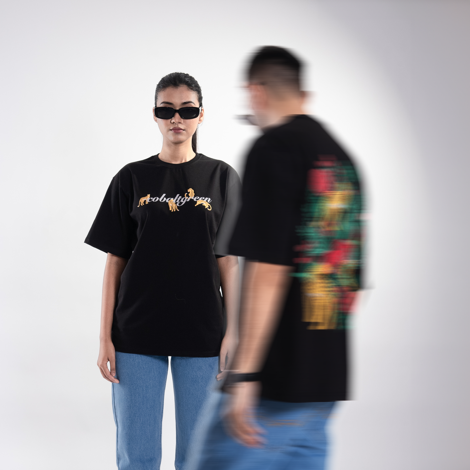 Male and female models, both 5'10", wearing the classic black 'Leopard Tee' in a posed shot, showcasing both the front and back designs. The front features a bold leopard and rose graphic, while the back mirrors the design with the same striking screen and puff print. The oversized, unisex fit offers a relaxed and flattering look for both models, embodying wild style and effortless comfort.