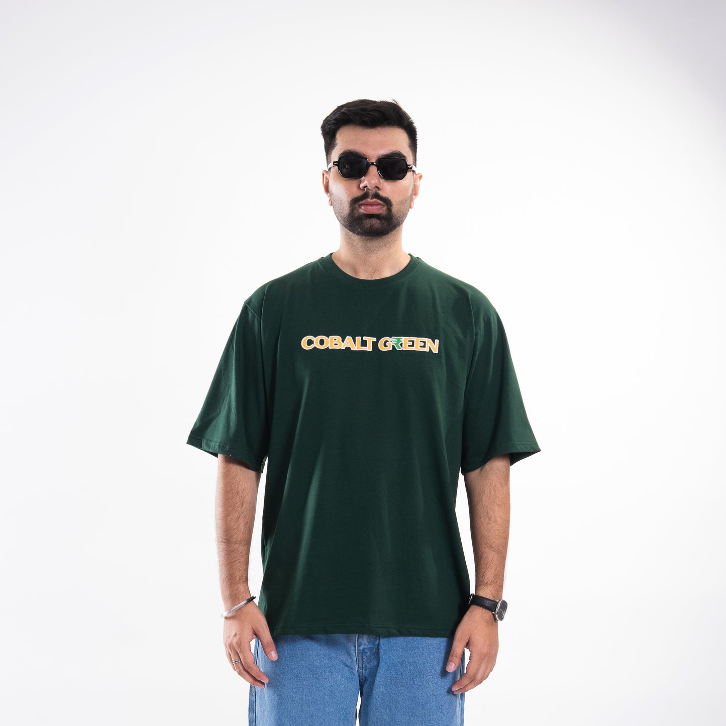 Male model, 5'10", wearing the deep dark green 'Expensive Tee' in a mid shot, showcasing the oversized fit. The front features subtle 'Cobalt Green' branding, highlighting the shirt's minimalist yet luxurious style. The comfort fit drapes effortlessly, making it perfect for a relaxed, fashion-forward look.