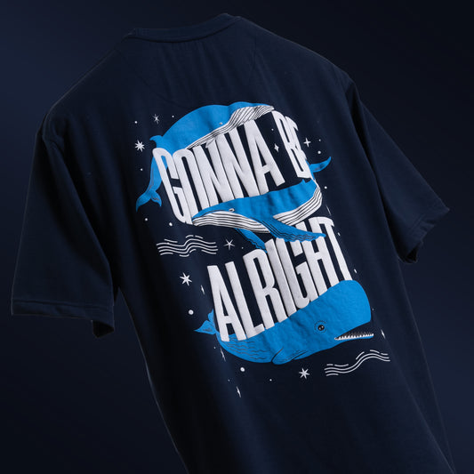 Deep navy blue oversized 'Gonna Be Alright Tee' floating against a matching backdrop, featuring 'Cobalt Green' branding on the front. The back showcases the uplifting phrase 'gonna be alright' with playful blue whale graphics in screen and puff print. Crafted from 220 GSM cotton-rich fabric with bio-washed and gold-finished treatment for a soft, premium feel. The tee's oversized, unisex design offers a relaxed fit, perfect for spreading positivity and comfort.