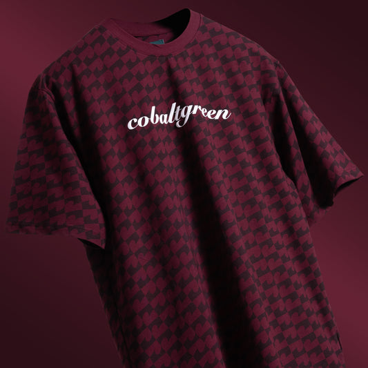 Maroon oversized t-shirt with an all-over-print design, floating against a matching maroon background for a tone-on-tone effect. The shirt features 'Cobalt green' branding on the chest plate, creating a subtle yet stylish look that emphasizes the seamless blend of color and design.