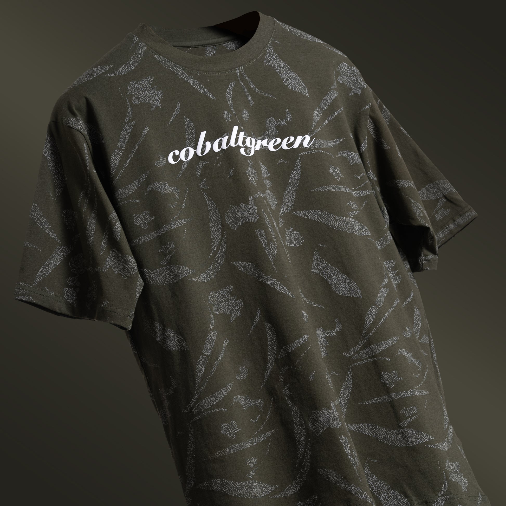 Olive oversized t-shirt with an all-over-print design, floating against a matching olive-toned background for a cohesive, monochromatic effect. The shirt is accented with 'Cobalt green' branding on the chest plate, offering a sleek and modern look.