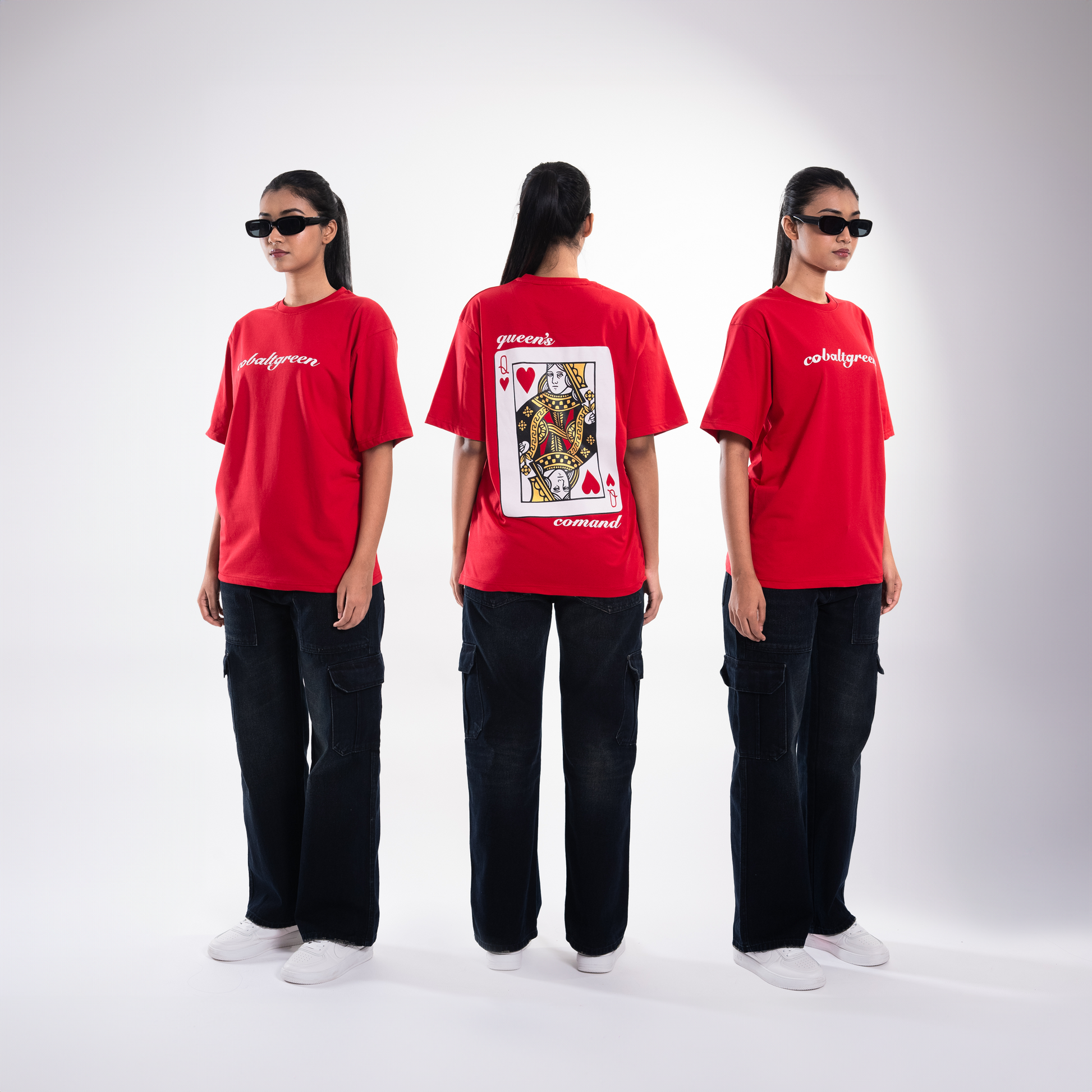 Female model wearing the red 'Queen's Command Tee' in a split frame showing the front, side, and back. The front features 'Cobalt Green' branding, while the back displays the bold 'Queen's Command' phrase and an illustrated Queen of Hearts card in screen and puff print. The split view highlights the oversized, unisex fit, offering a relaxed and flattering look from multiple angles, showcasing both the striking design and premium comfort.