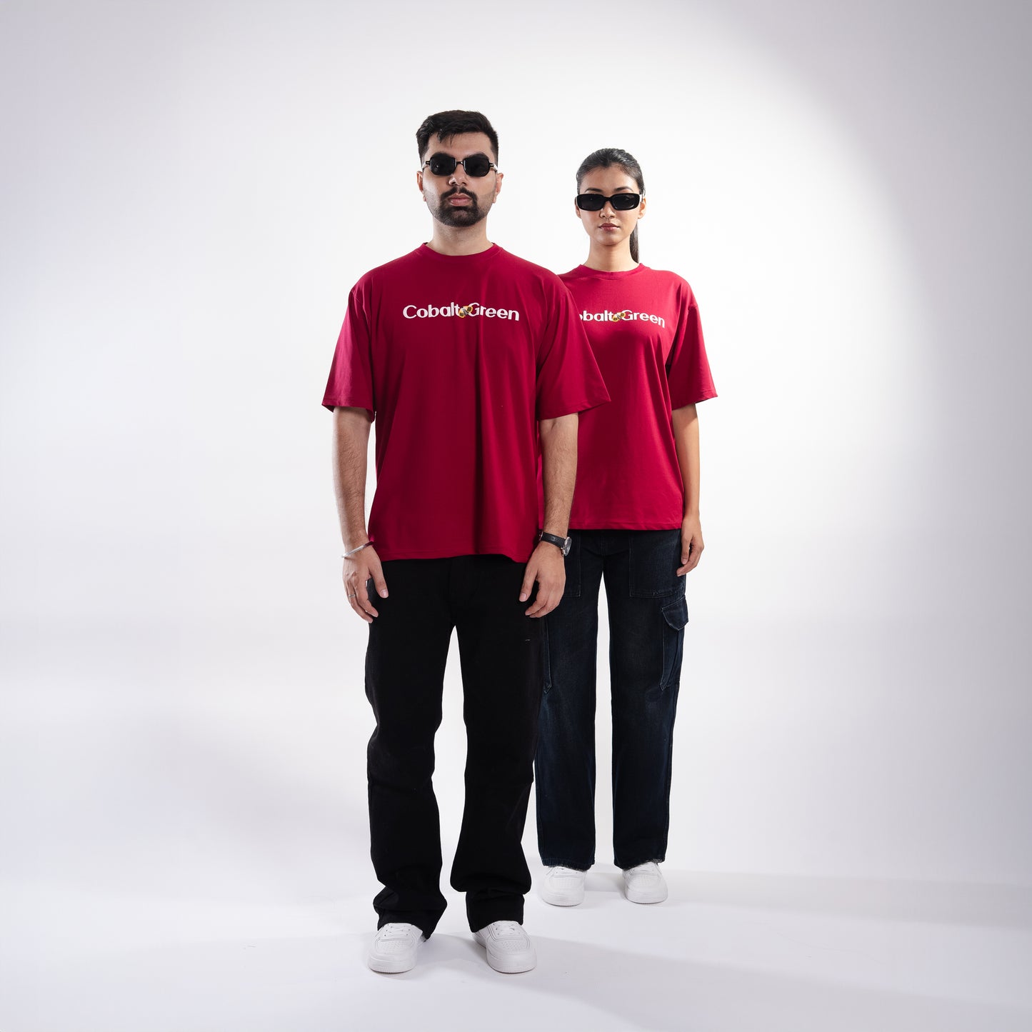 Male and female models, both 5'10", wearing the bold maroon 'Stop Bugging Me Tee' in a posed front shot. The front of the tee features 'Cobalt Green' branding, while the oversized fit provides a relaxed and flattering look. The playful design combines humor and comfort, making it a stylish statement piece for both models, perfect for casual outings or expressing a bit of attitude.