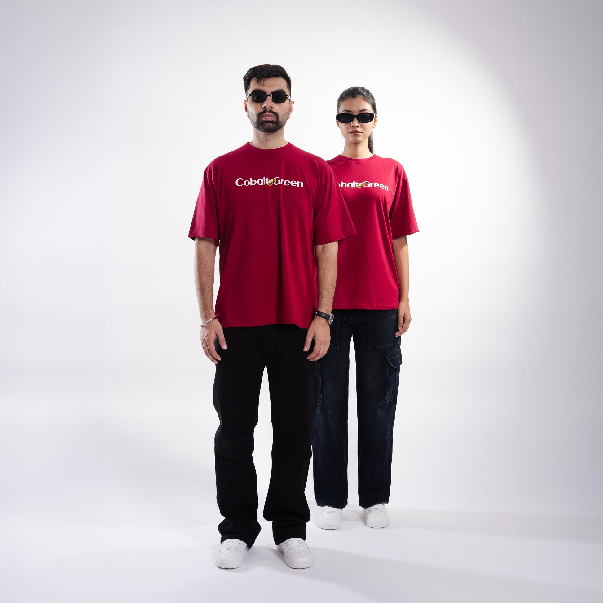 Male and female models, both 5'10", wearing the bold maroon 'Stop Bugging Me Tee' in a posed front shot. The front of the tee features 'Cobalt Green' branding, while the oversized fit provides a relaxed and flattering look. The playful design combines humor and comfort, making it a stylish statement piece for both models, perfect for casual outings or expressing a bit of attitude.
