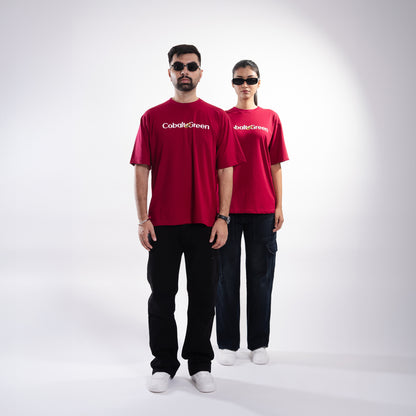 Male and female models, both 5'10", wearing the bold maroon 'Stop Bugging Me Tee' in a posed front shot. The front of the tee features 'Cobalt Green' branding, while the oversized fit provides a relaxed and flattering look. The playful design combines humor and comfort, making it a stylish statement piece for both models, perfect for casual outings or expressing a bit of attitude.