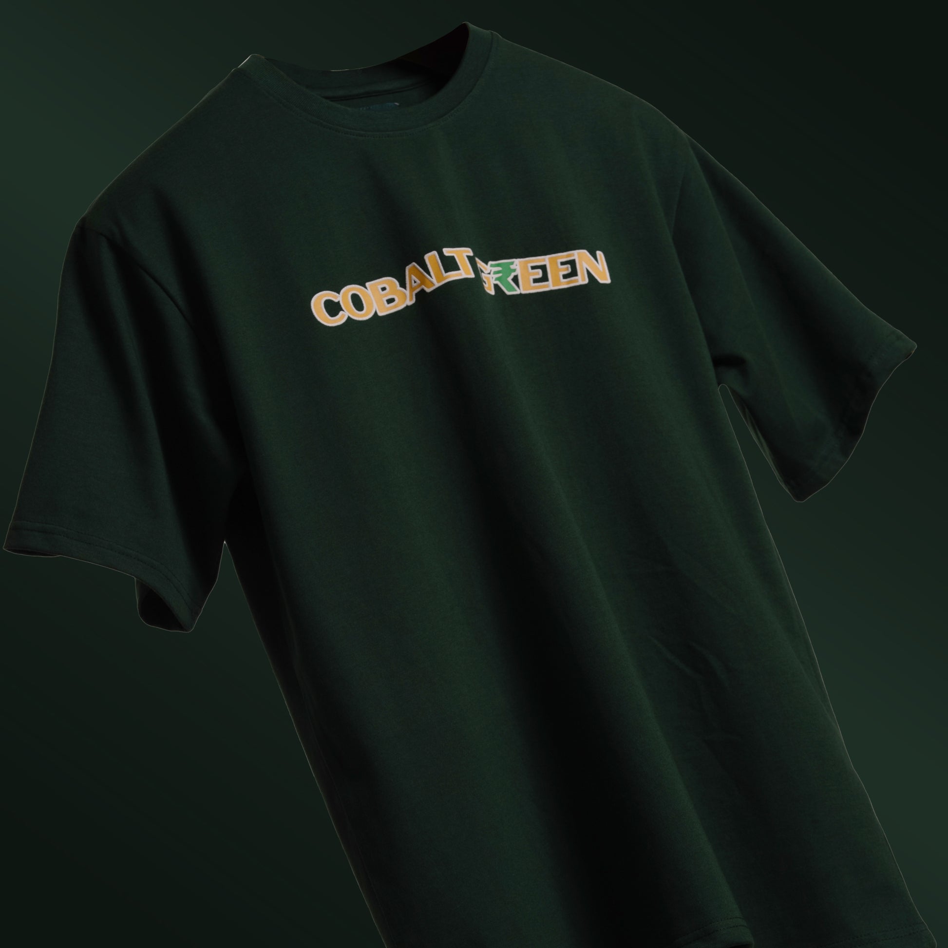 Deep dark green oversized 'Expensive Tee' floating against a matching background, featuring 'Cobalt Green' branding on the front. The back is adorned with bold screen and puff print reading 'Expensive' accented with currency symbols, adding a luxe, streetwear vibe. Made from 220 GSM cotton-rich fabric with bio-washed and gold-finished treatment for a soft, premium feel. Designed for a relaxed unisex fit, blending casual comfort with high-end style.