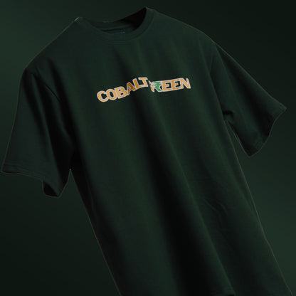 Deep dark green oversized 'Expensive Tee' floating against a matching background, featuring 'Cobalt Green' branding on the front. The back is adorned with bold screen and puff print reading 'Expensive' accented with currency symbols, adding a luxe, streetwear vibe. Made from 220 GSM cotton-rich fabric with bio-washed and gold-finished treatment for a soft, premium feel. Designed for a relaxed unisex fit, blending casual comfort with high-end style.