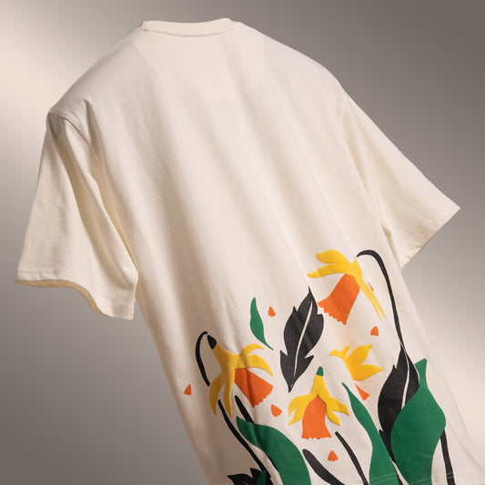 Off-white oversized 'Yellow Lily Tee' floating against a matching backdrop, featuring beautiful yellow summer lilies in screen and puff print on the front and back. Crafted from 220 GSM cotton-rich fabric with bio-washed and gold-finished treatment for a soft, premium feel. The unisex comfort fit offers a relaxed, flattering look, making this tee perfect for casual outings, weekend wear, or lounging in style.