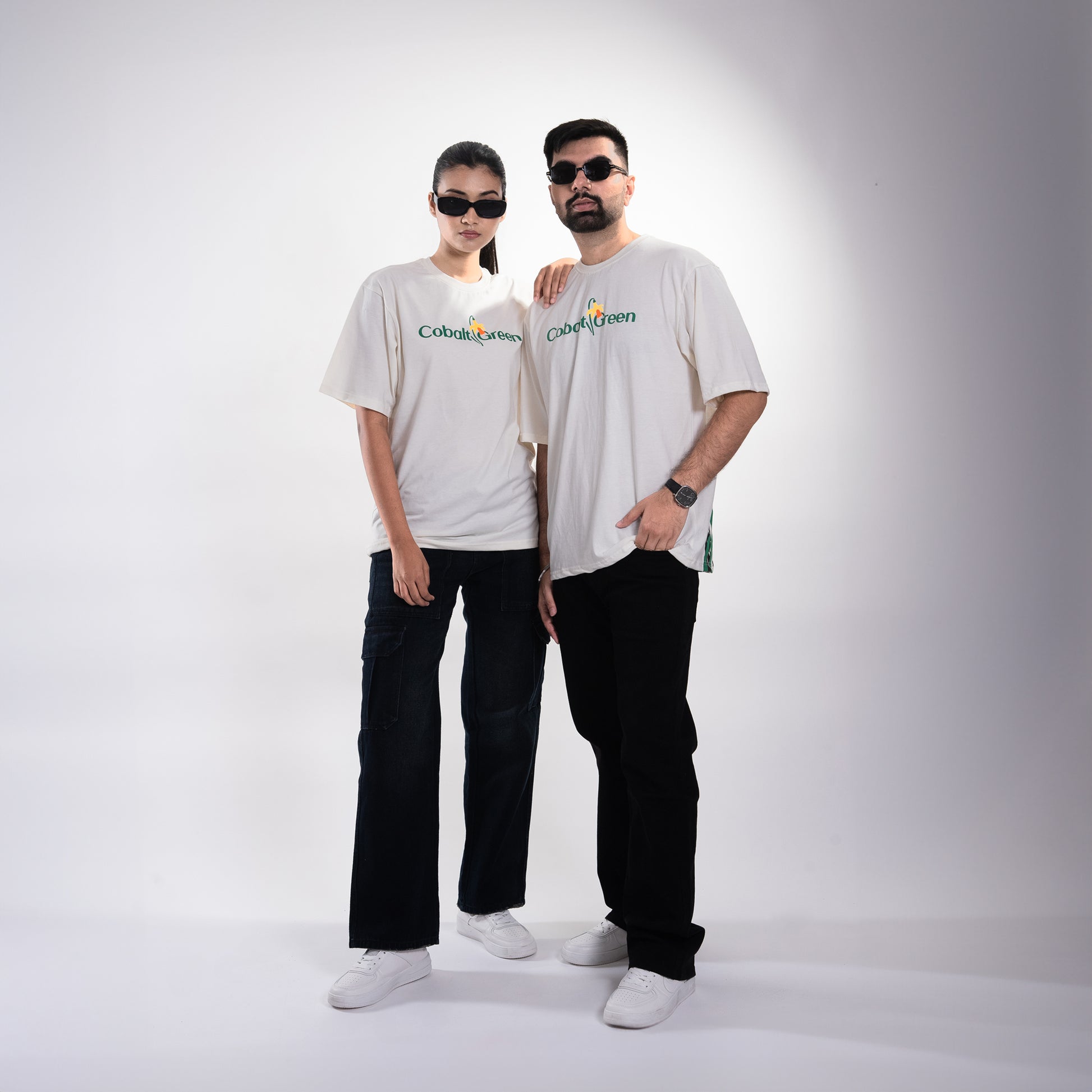 Male and female models, both 5'10", wearing the off-white 'Yellow Lily Tee' in a posed front shot. The tee features vibrant yellow summer lilies in screen and puff print on the front and back. The oversized, unisex fit provides a relaxed and flattering look for both models, showcasing the floral design and premium craftsmanship of the tee.