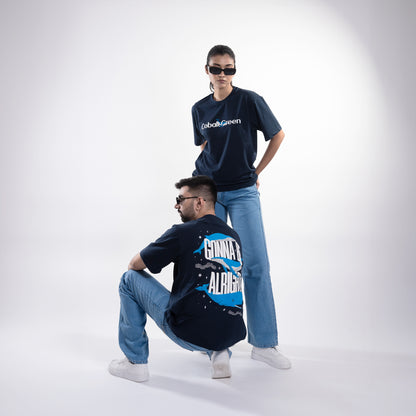 Male and female models, both 5'10", wearing the deep navy blue 'Gonna Be Alright Tee' in a posed shot. The front features 'Cobalt Green' branding, while the back showcases the uplifting 'gonna be alright' phrase with playful blue whale graphics. The oversized fit and unisex design create a relaxed, stylish look that flatters both body types, emphasizing comfort and positive vibes.