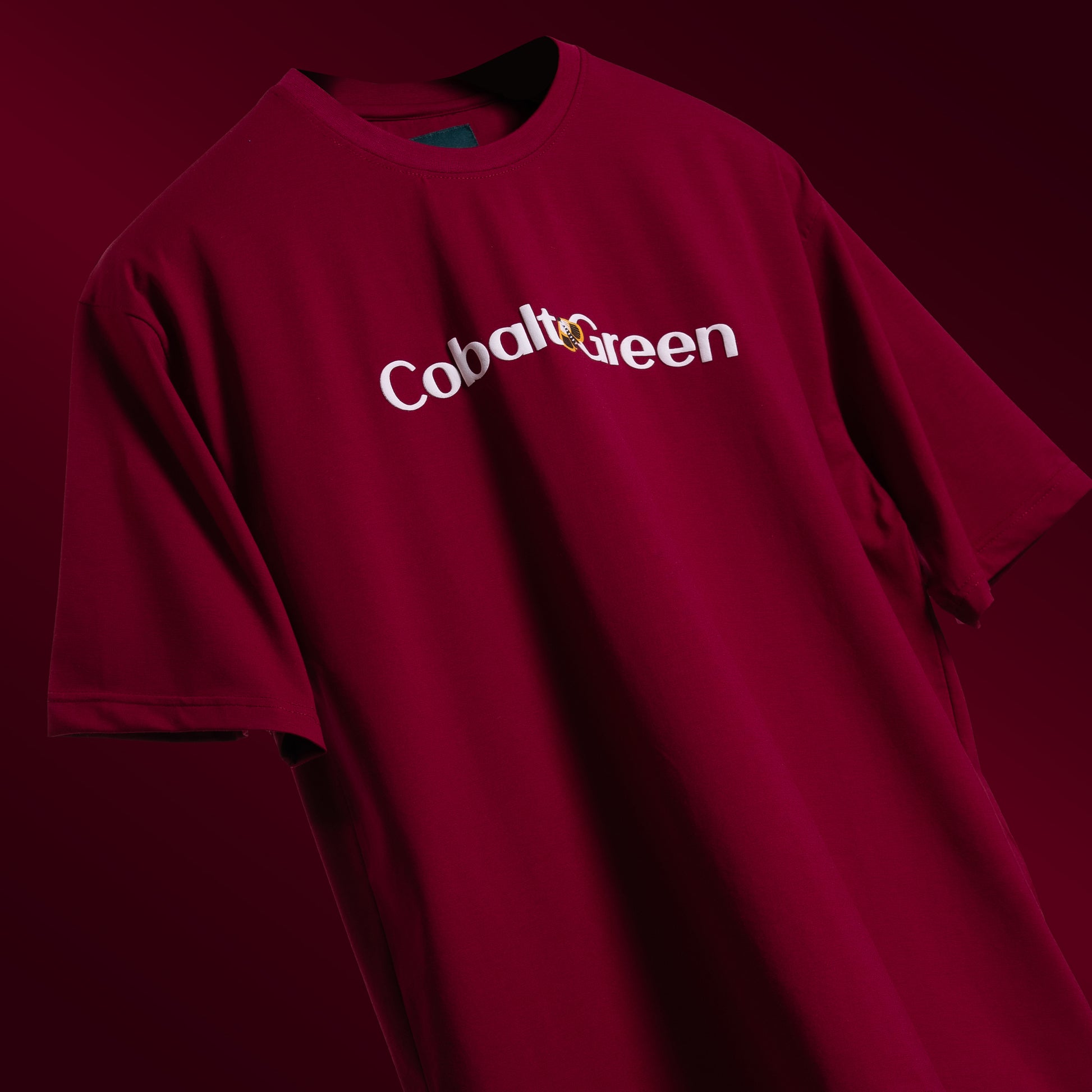 Bold maroon oversized 'Stop Bugging Me Tee' floating against a matching backdrop, featuring 'Cobalt Green' branding on the front. The back displays the playful 'STOP BUGGING ME' phrase with quirky bug graphics in screen and puff print. Made from 220 GSM cotton-rich fabric with bio-washed and gold-finished treatment for a soft, premium feel. The oversized, unisex design ensures comfort and style for all, perfect for casual wear with a sassy attitude.