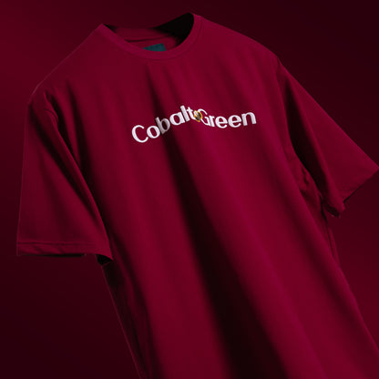 Bold maroon oversized 'Stop Bugging Me Tee' floating against a matching backdrop, featuring 'Cobalt Green' branding on the front. The back displays the playful 'STOP BUGGING ME' phrase with quirky bug graphics in screen and puff print. Made from 220 GSM cotton-rich fabric with bio-washed and gold-finished treatment for a soft, premium feel. The oversized, unisex design ensures comfort and style for all, perfect for casual wear with a sassy attitude.