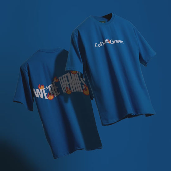 Video showcasing two oversized 'We're Enemies Tees' floating against a matching royal blue backdrop, rotating to display both the front and back of the tee. The front features 'Cobalt Green' branding, while the back highlights the bold 'We're Enemies' phrase with dynamic fire symbols in screen and puff print. The video emphasizes the oversized, unisex fit and bold, edgy design, perfect for adding attitude to any casual look.