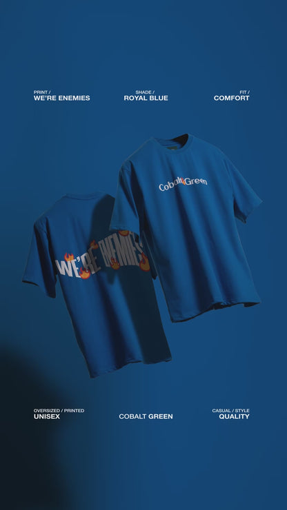 Video showcasing two oversized 'We're Enemies Tees' floating against a matching royal blue backdrop, rotating to display both the front and back of the tee. The front features 'Cobalt Green' branding, while the back highlights the bold 'We're Enemies' phrase with dynamic fire symbols in screen and puff print. The video emphasizes the oversized, unisex fit and bold, edgy design, perfect for adding attitude to any casual look.