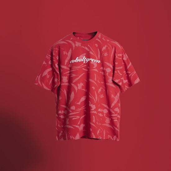 Video of a brick-red oversized t-shirt with an all-over-print design, floating gracefully against an orange background. Text overlays highlight key features: 'Cobalt green' branding on the chest, premium fabric, and relaxed fit. A dynamic showcase emphasizing its unique style and comfort.