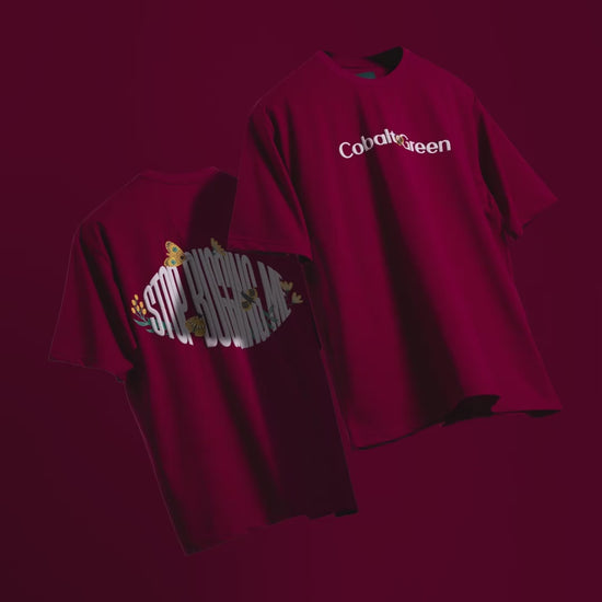 Video showcasing two oversized 'Stop Bugging Me Tees' floating against a matching maroon backdrop, rotating to display both the front and back. The front features 'Cobalt Green' branding, while the back highlights the fun 'STOP BUGGING ME' phrase and quirky bug graphics in screen and puff print. The video emphasizes the oversized, unisex fit and playful design, perfect for a relaxed yet bold look.